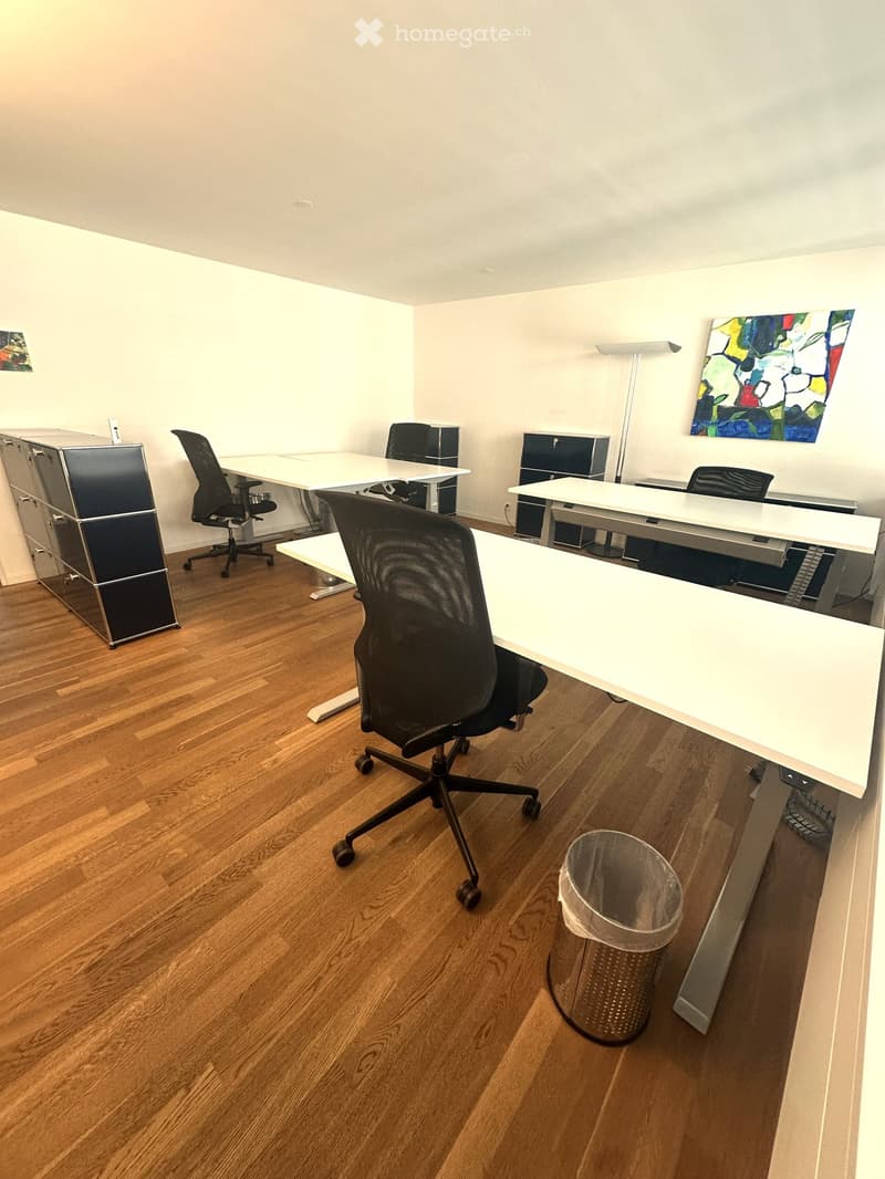 Office space with wooden flooring, white tables, black chairs, a cabinet, a floor lamp, and a trash can.