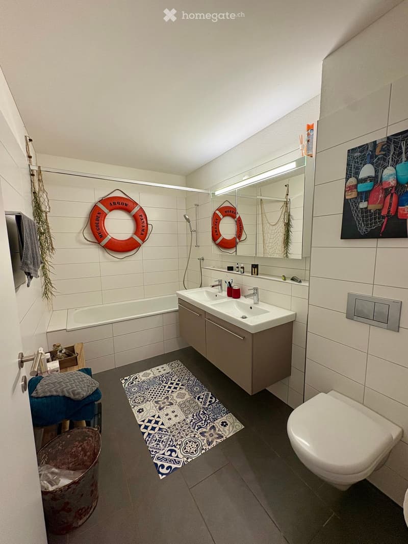 Modern bathroom with a bathtub, sink, toilet, mirror, and decorative elements including a lifebuoy and a plant.