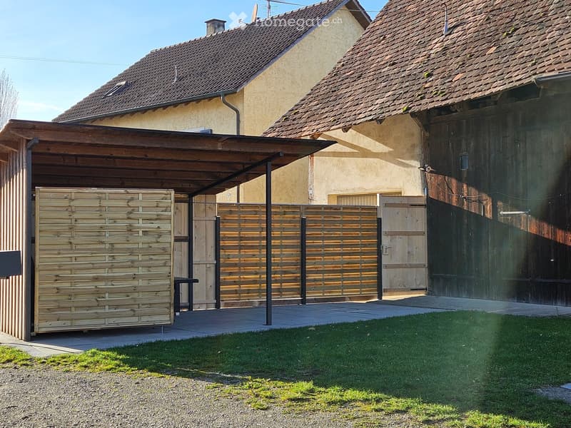 A wooden garage with a covered entrance, surrounded by a wooden fence and a grassy lawn.