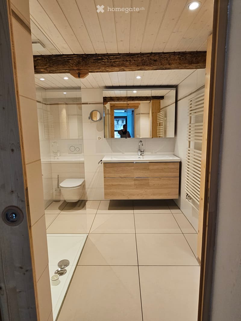 small bathroom with glass shower, toilet, sink, large mirror, wooden vanity, white tiles