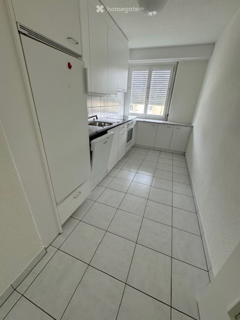 Modern kitchen with white cabinets, tiled floor, and a sink with a dishwasher underneath.