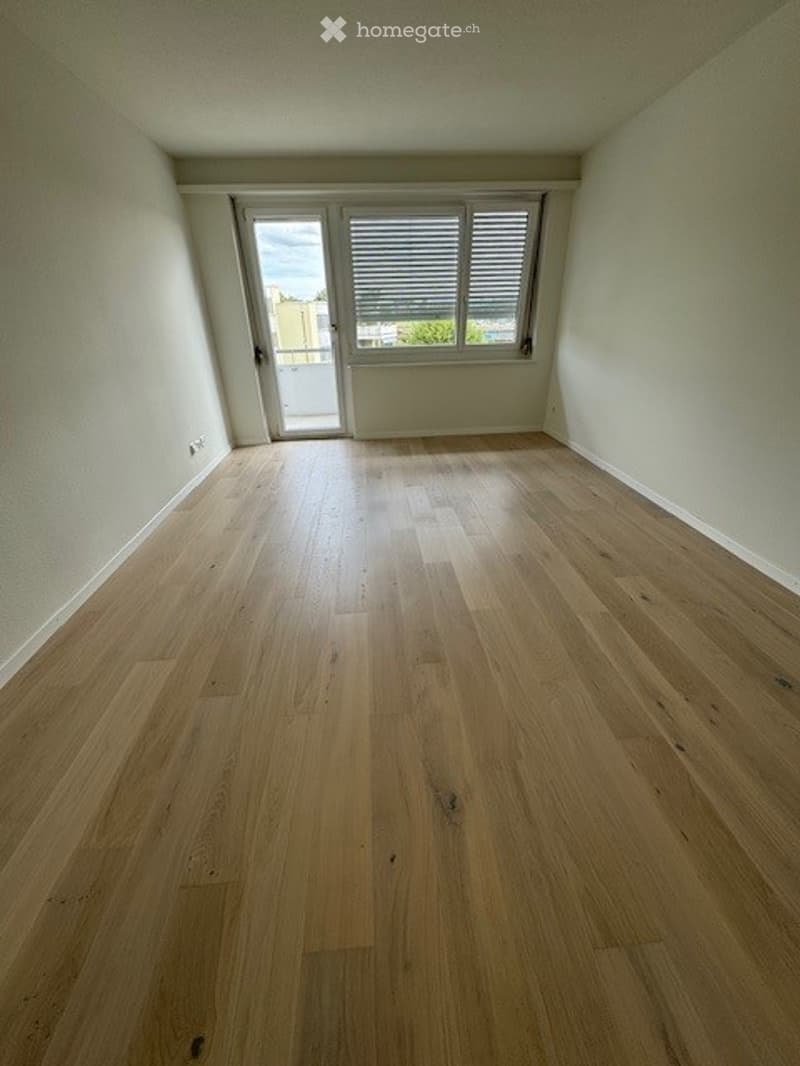 Empty room with light wooden flooring, white walls, and a large window with blinds. No furniture or equipment present.