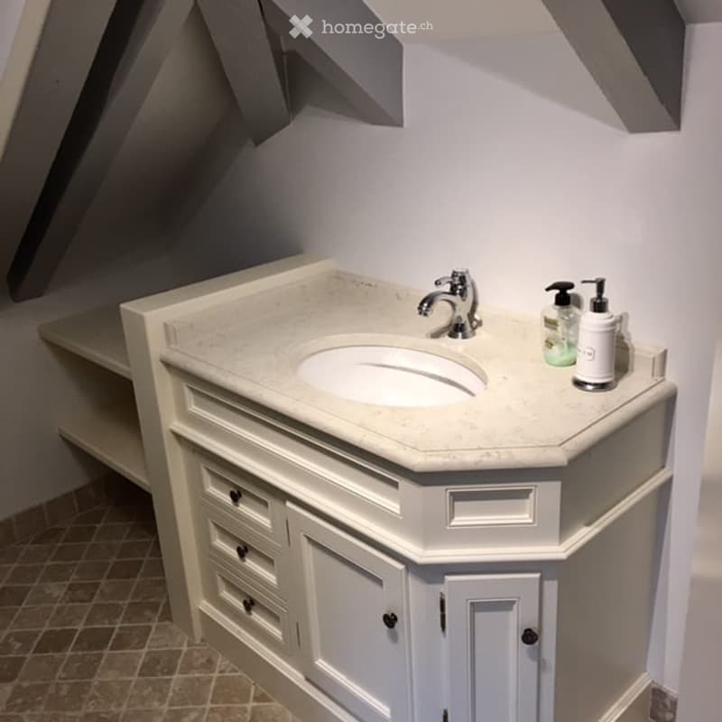 Modern bathroom with a corner sink, white cabinetry, marble countertop, and built-in shelving.
