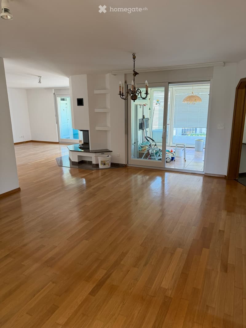 Empty room with polished wooden flooring, white walls, and large sliding glass doors leading to a balcony area.