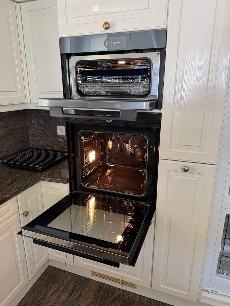 Modern kitchen with white cabinets and a built-in oven with multiple compartments, all doors open to show the interior.