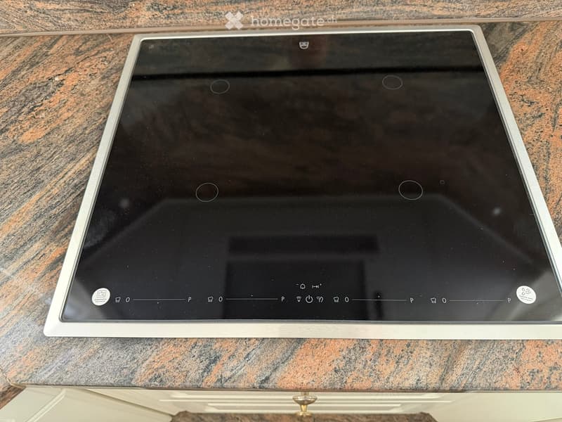 Modern induction cooktop with touch controls, placed on a marble countertop.