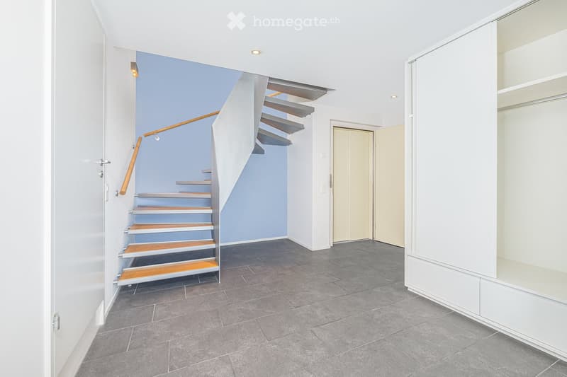 Empty hallway with tiled floor, blue wall, wooden handrail, and a modern staircase.