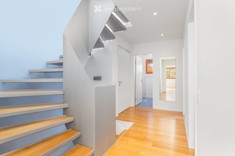 Modern hallway with wooden floor, white walls, and a spiral staircase with blue accent wall.