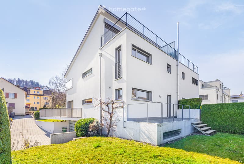 Modern white house with multiple windows, a balcony, and a driveway.