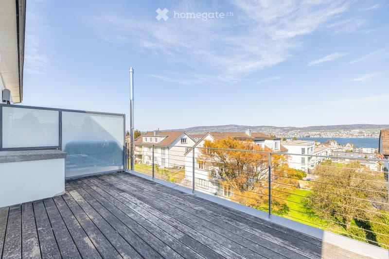 A balcony with a wooden floor, glass railings, and a view of the city and lake.