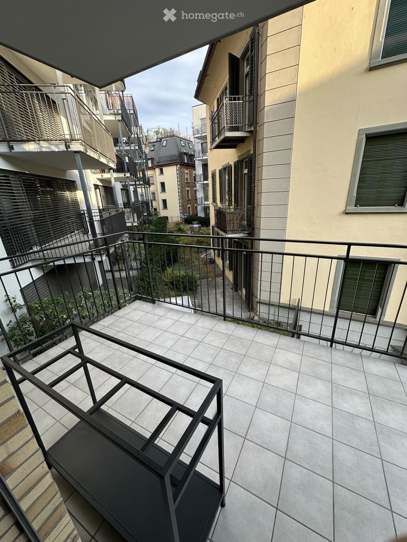 Balcony with tiled floor, metal railing, and view of neighboring buildings and greenery.