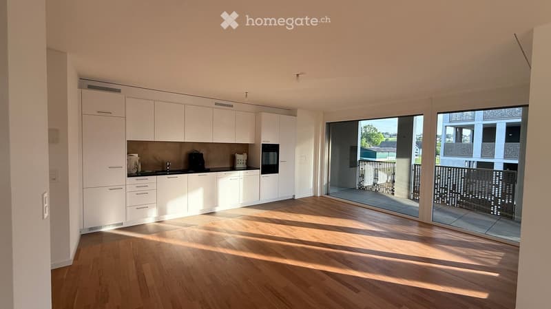 Modern kitchen with white cabinets, wooden flooring, and large windows offering a view of the outdoor area.
