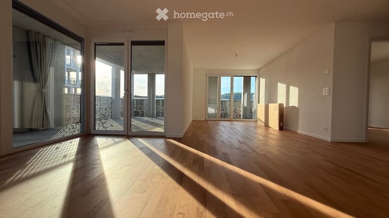 Empty room with wooden flooring, large windows, and sliding glass doors leading to a balcony.
