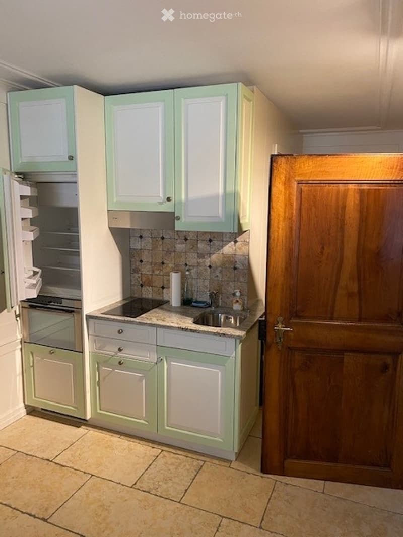A modern kitchen with light green cabinets, a stainless steel sink, and a built-in oven. The countertop is tiled, and the floor is made of beige tiles.