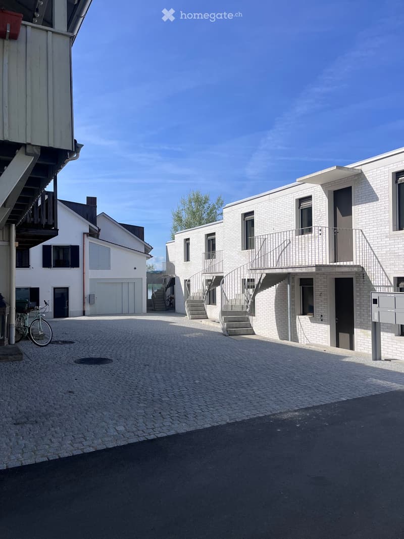 Modern residential complex with white brick buildings, balconies, and a paved courtyard.