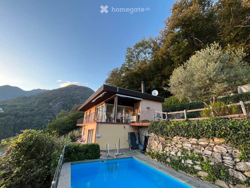 A modern two-story house with a balcony, surrounded by lush greenery and a swimming pool, overlooking a scenic mountainous landscape.