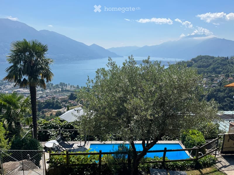 A scenic outdoor area with a swimming pool, surrounded by lush greenery, overlooking a lake and mountains.