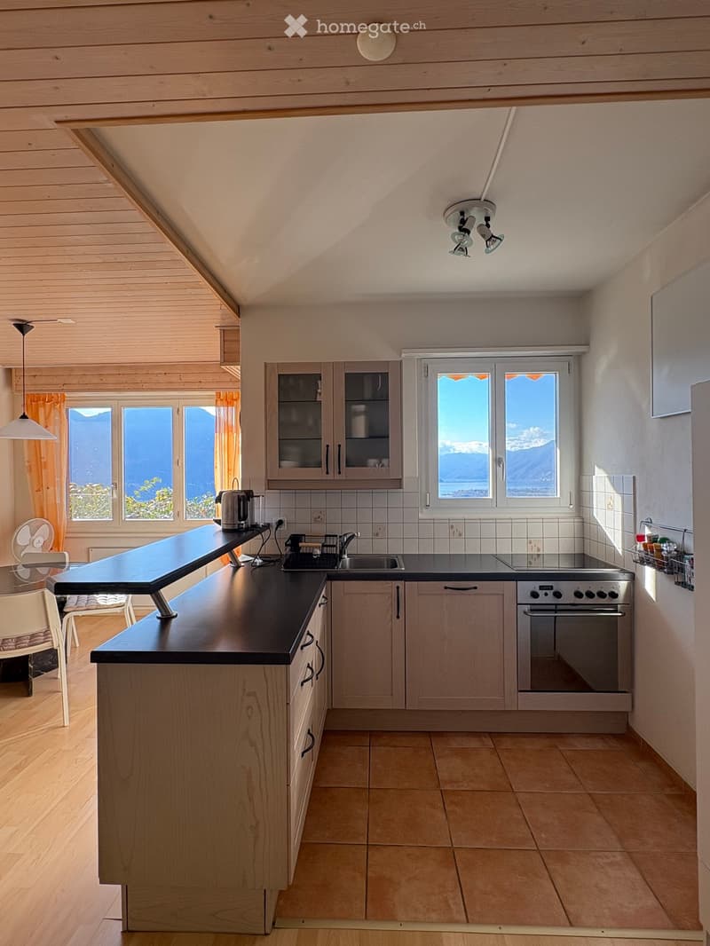 Modern kitchen with wooden cabinets, black countertop, stainless steel appliances, and large windows overlooking a scenic mountain view.