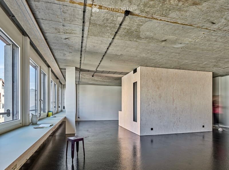 Minimalist room with large windows, polished concrete floor, exposed concrete ceiling, and a small wooden stool near the window.