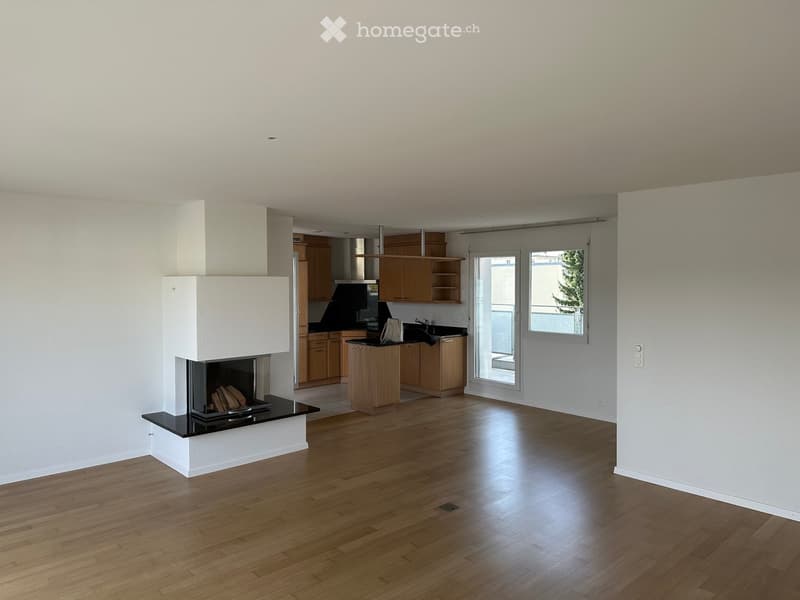 Open-plan living and kitchen area with wooden flooring, a modern fireplace, and light wooden kitchen cabinets.