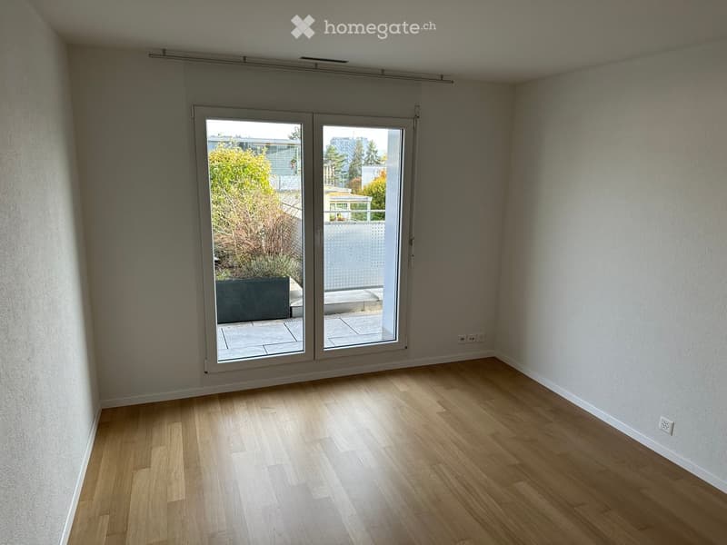 Empty room with wooden flooring, white walls, and large sliding glass doors leading to a balcony or terrace area.