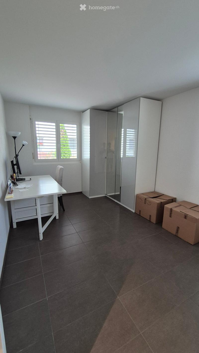 A furnished room with a desk, chair, lamp, wardrobe, mirror, and screen. The room has dark tiled flooring and white walls.