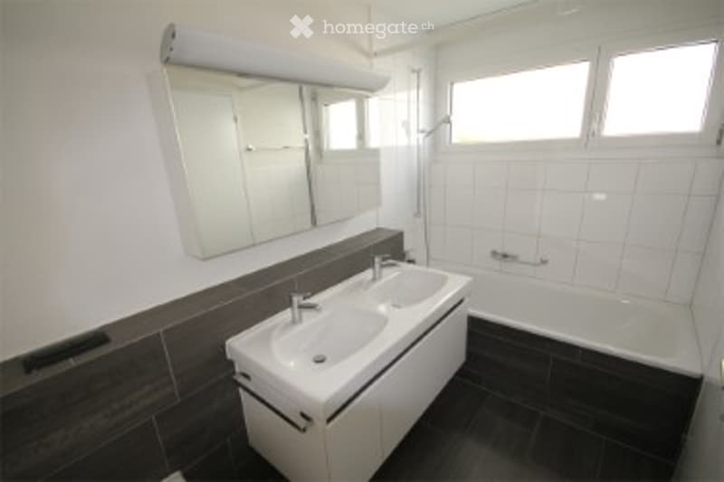 Modern bathroom with white tiles, dark wood accents, a large mirror, a sink with a modern faucet, and a bathtub.