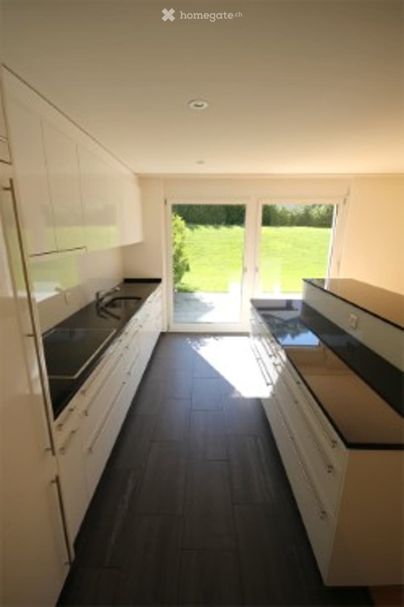 Modern kitchen with white cabinets, dark tiled floor, and a large window offering a view of the garden.