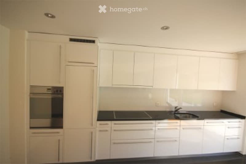 Modern kitchen with white cabinets, black countertops, and built-in oven. Features a sleek, minimalist design with a central island and ample storage space.