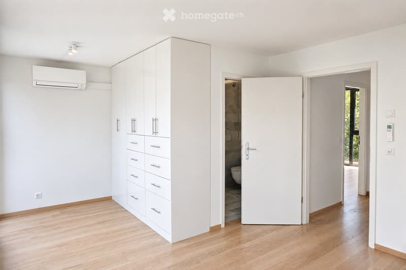 Empty room with light wooden flooring, white walls, built-in white cabinetry, and an open doorway leading to a bathroom.