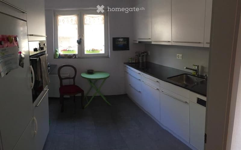Modern kitchen with white cabinets, stainless steel sink, and a small round table with a chair near the window.