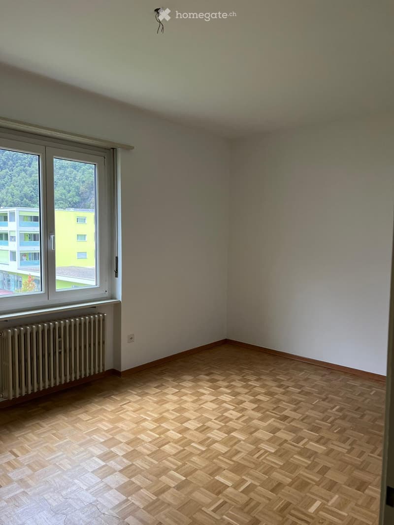 Empty room with white walls, large window, and hardwood parquet flooring.