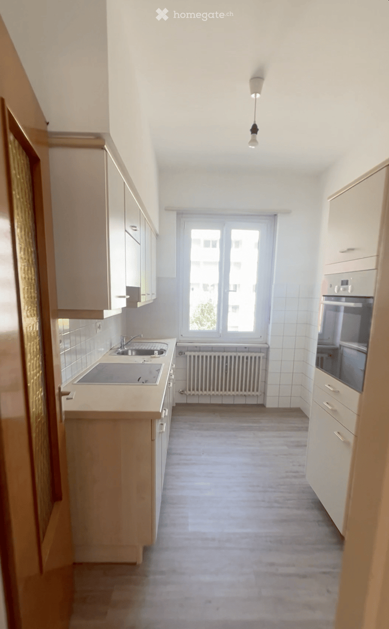 Galley-style kitchen with white cabinets, tile backsplash, stainless steel appliances including a dishwasher, and a window providing natural light