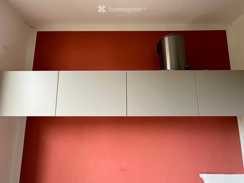 Modern kitchen with white and red cabinets, a stainless steel trash can on top, and a sleek design.