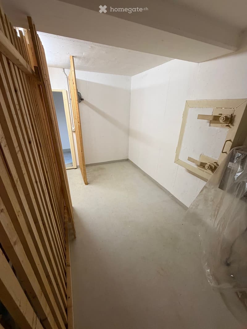 Empty room with white walls and concrete floor, featuring a partially constructed wooden door frame and a doorway leading to another room.