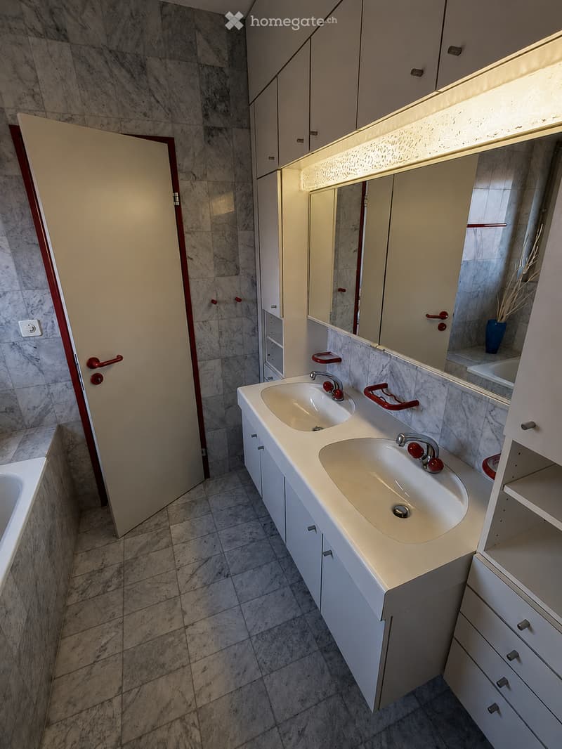 Modern bathroom with double sink, white cabinets, marble tiles, and a large mirror with built-in lighting.