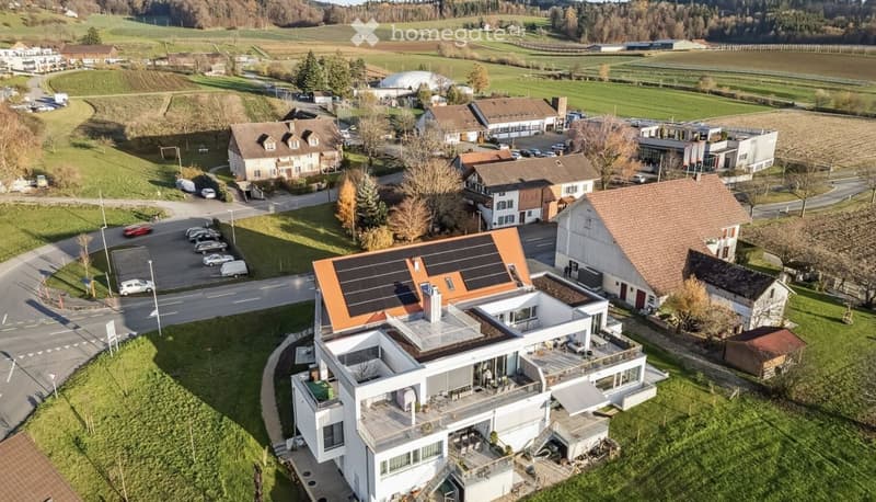 Modern house with solar panels, multiple balconies, surrounded by other houses and greenery