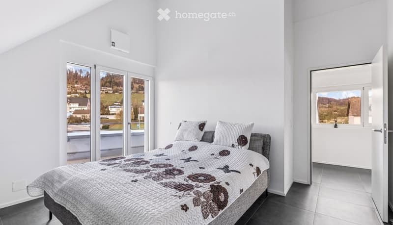 modern bedroom with white walls, gray floor, large bed with floral bedspread, two white pillows, large glass doors leading to balcony, scenic view