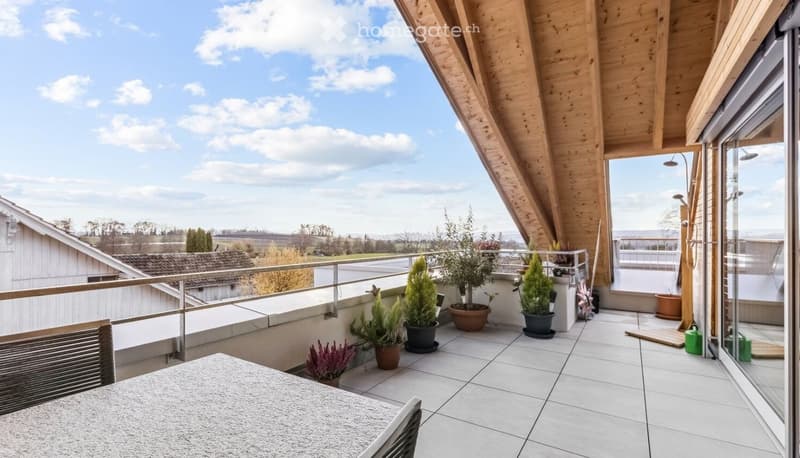 Balcony with wooden ceiling, white tiles, table, chairs, potted plants, railings, view of the sky and landscape