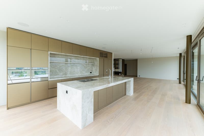 Modern kitchen with a large central island, sleek cabinetry, and a marble countertop. The space features light wooden flooring and recessed ceiling lighting.