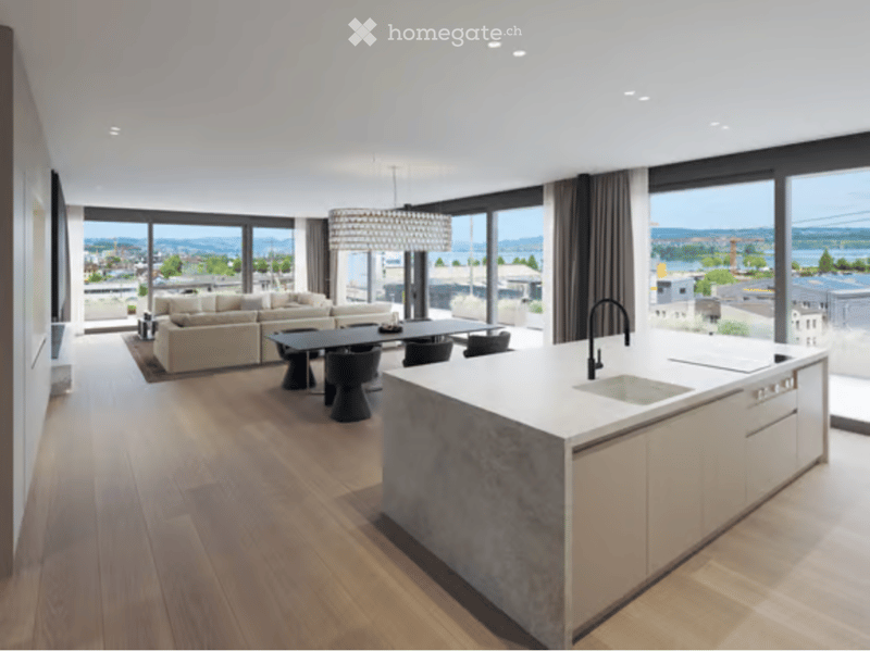 Modern open-plan living and dining area with a white kitchen island, sleek black faucet, and large windows offering a scenic view.