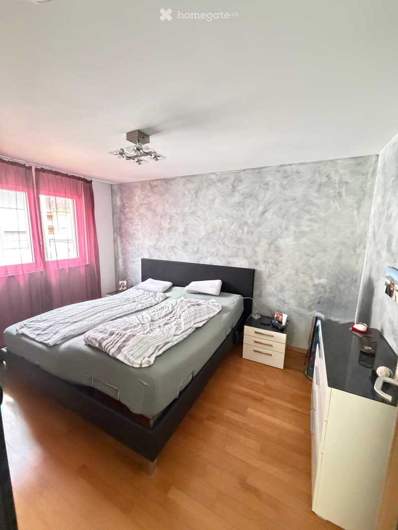 Modern bedroom with a double bed, nightstand, mirror, and wooden flooring.