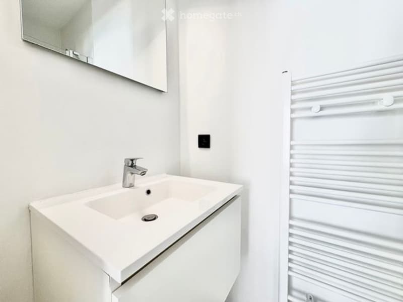 Modern bathroom with a white sink, chrome faucet, large mirror, and a white radiator.