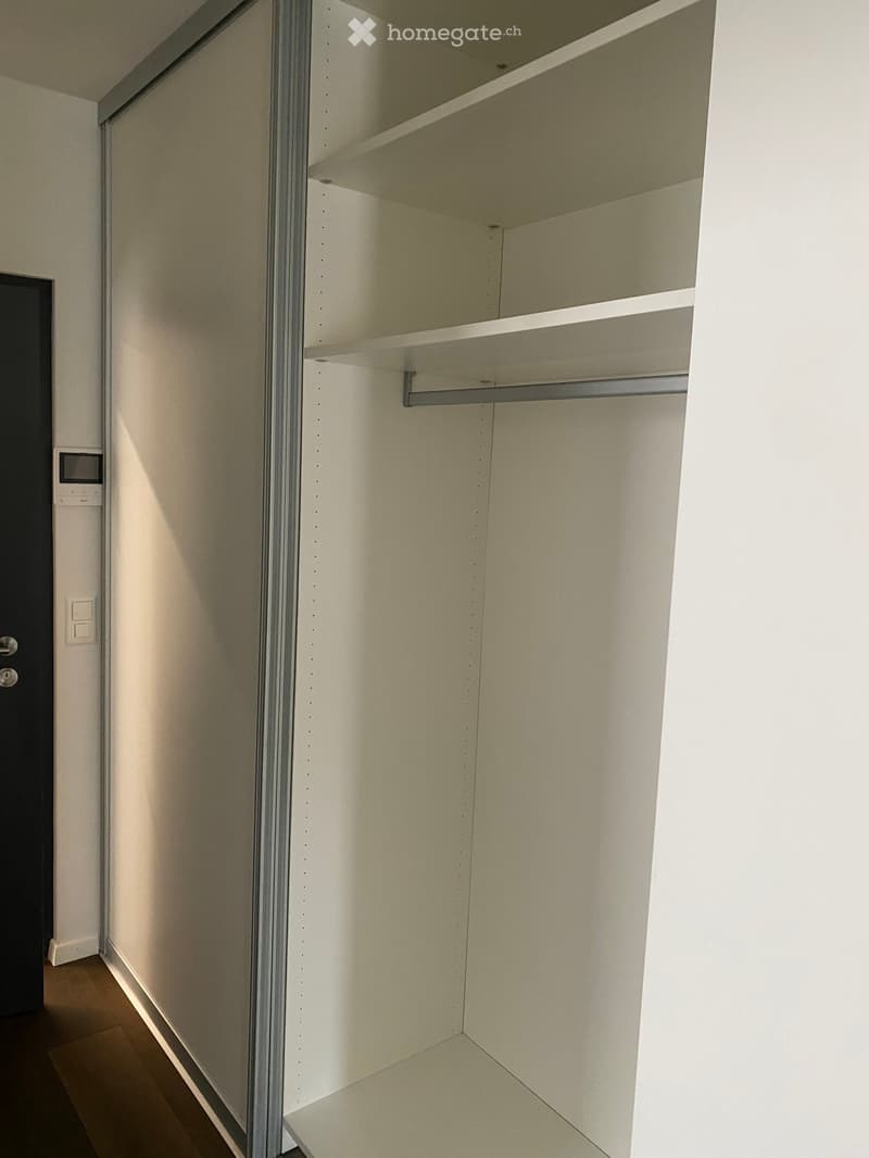 Empty closet with white walls, wooden floor, and built-in shelves and hanging rod.