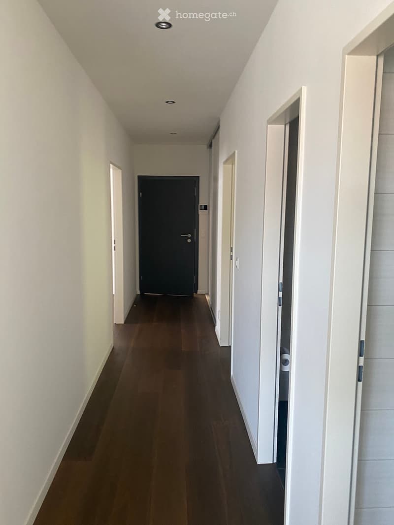Clean, modern hallway with wooden flooring, white walls, and several open doors leading to rooms.