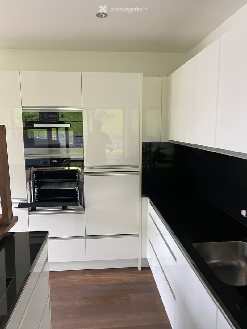 Modern kitchen with white cabinets, black countertops, and a wooden floor. Features an oven and a sink.