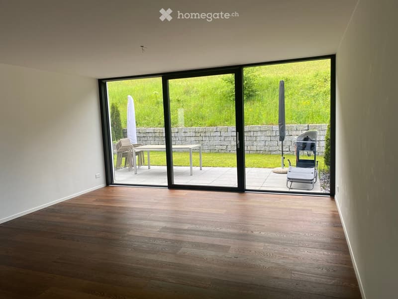 Empty room with wooden flooring and large sliding glass doors leading to a patio area with outdoor furniture.