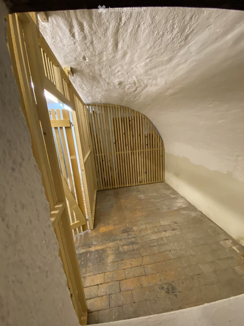 A narrow, arched stone staircase with wooden railings and a worn brick floor, leading upwards.