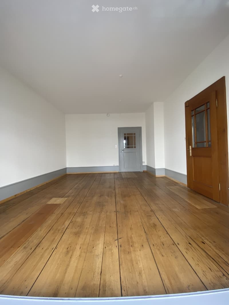 Empty room with wooden flooring, white walls, and two doors (one wooden and one grey).