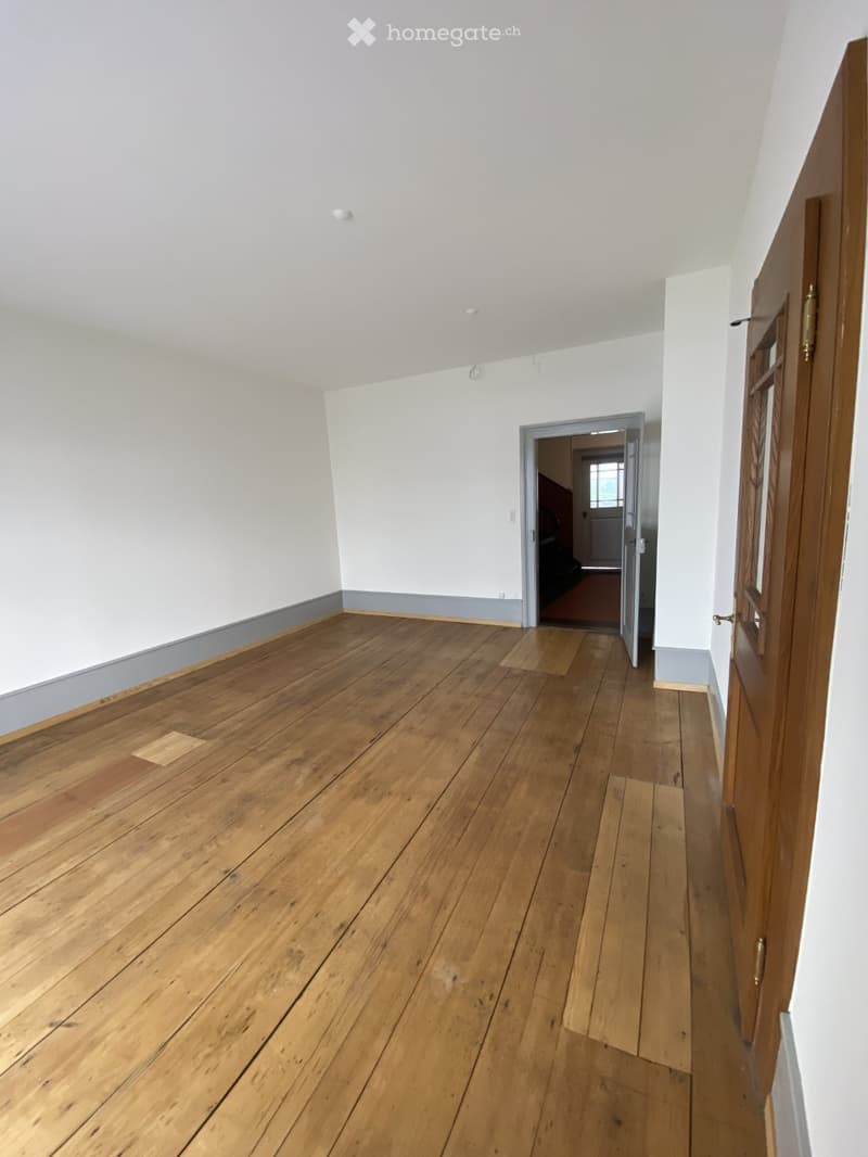 Empty room with wooden flooring and white walls, featuring a doorway leading to another room.